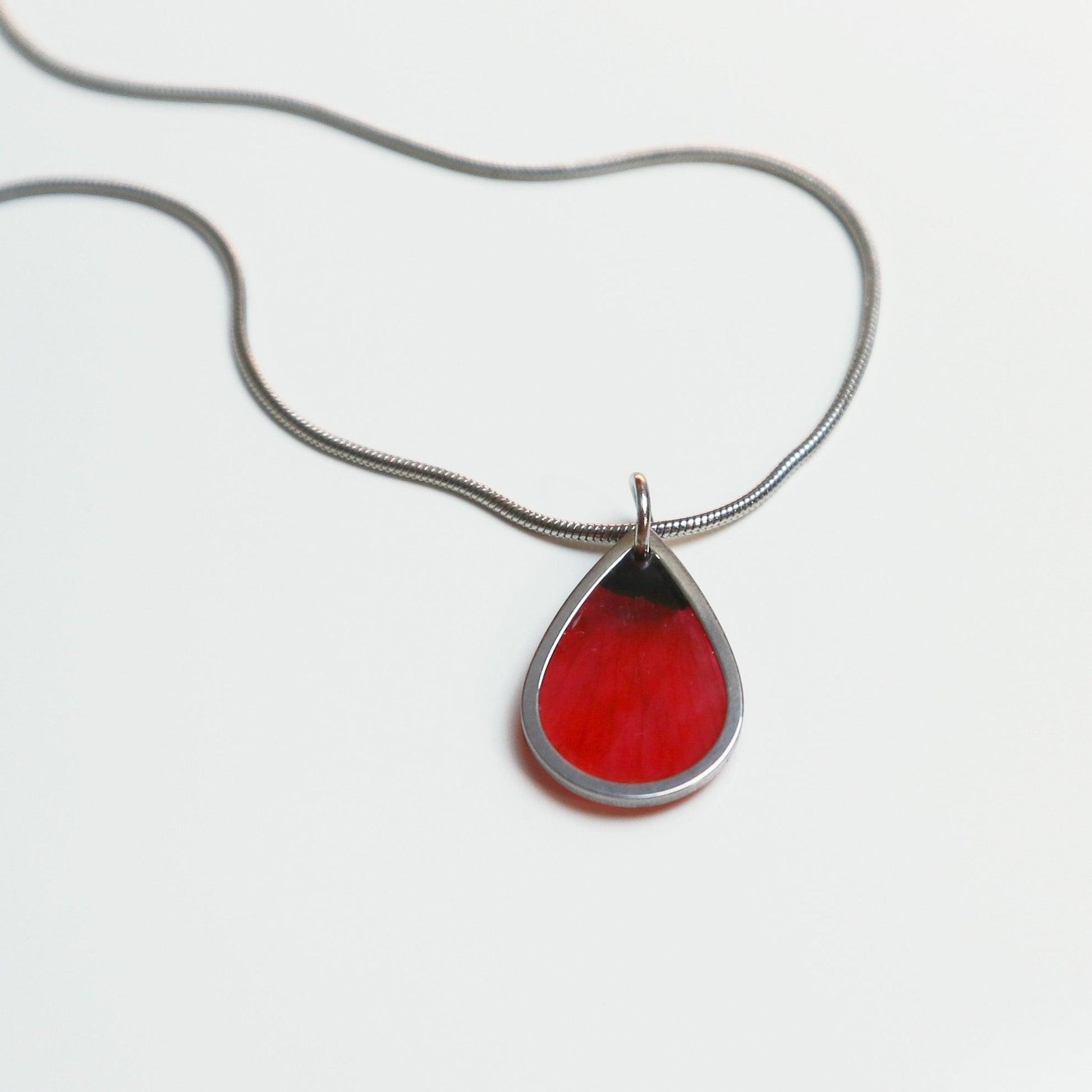 Drupt zilveren ketting met minimalistische druppelvormige hanger en een echte rode klaproos bloemblaadje erin.