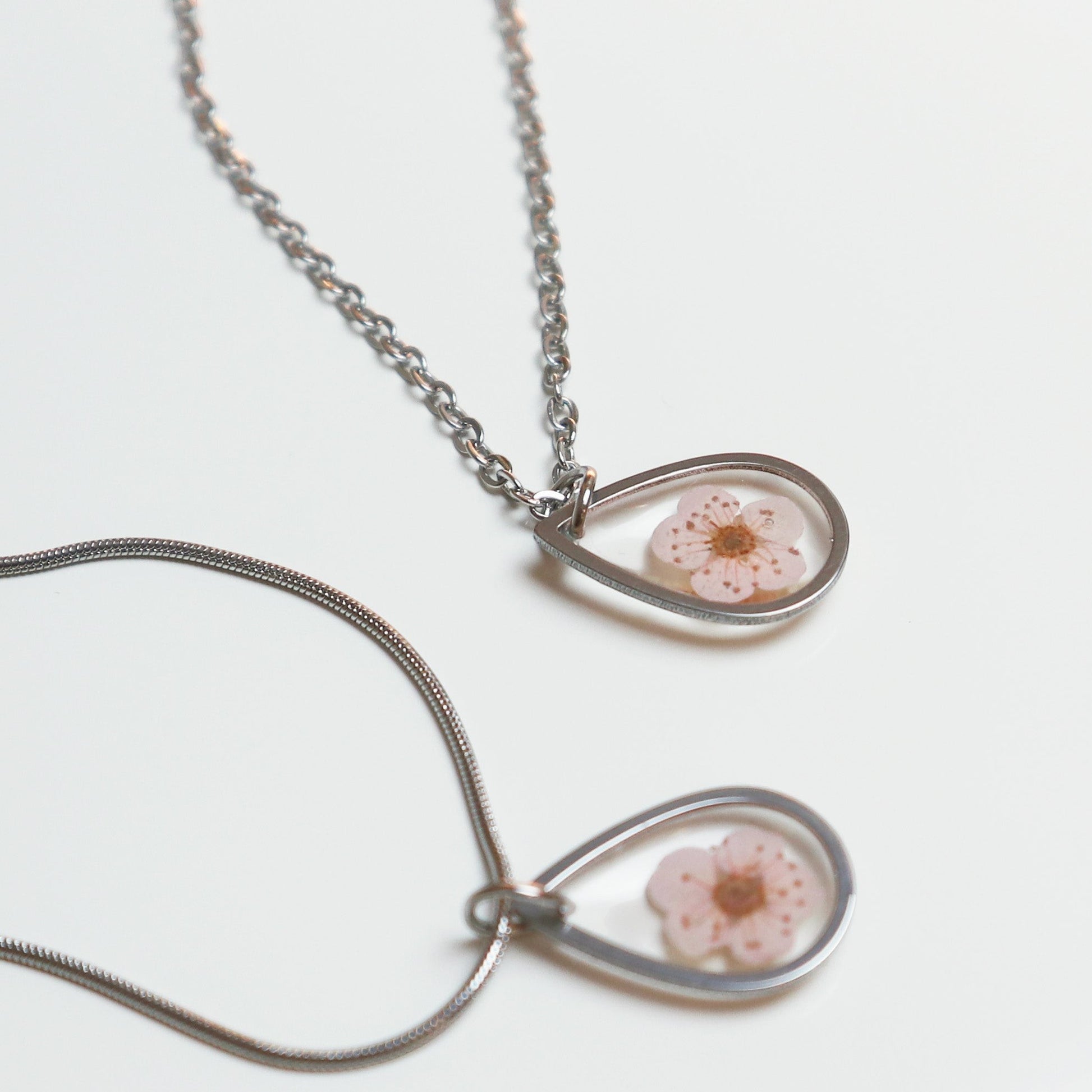 Drupt zilveren ketting met een druppelvormige hanger waarin een echte roze pruimenbloesem is verwerkt.