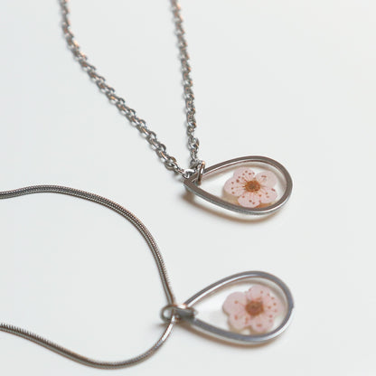 Drupt zilveren ketting met een druppelvormige hanger waarin een echte roze pruimenbloesem is verwerkt.