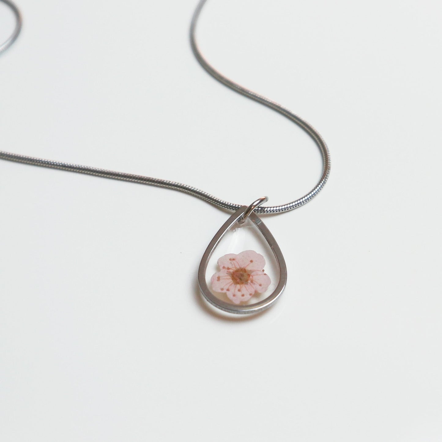 Drupt ketting met een zilveren druppelvormige hanger en een delicate roze pruimenbloesem erin verwerkt.