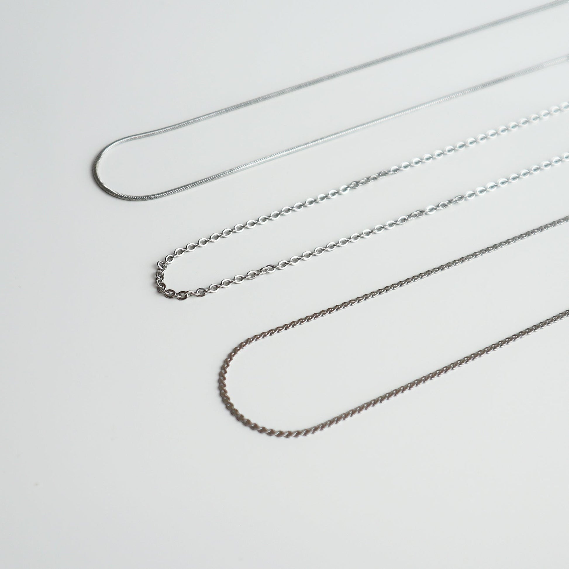 Drie verschillende zilverkleurige kettingen van Drupt op een witte achtergrond voor bij een hanger.
