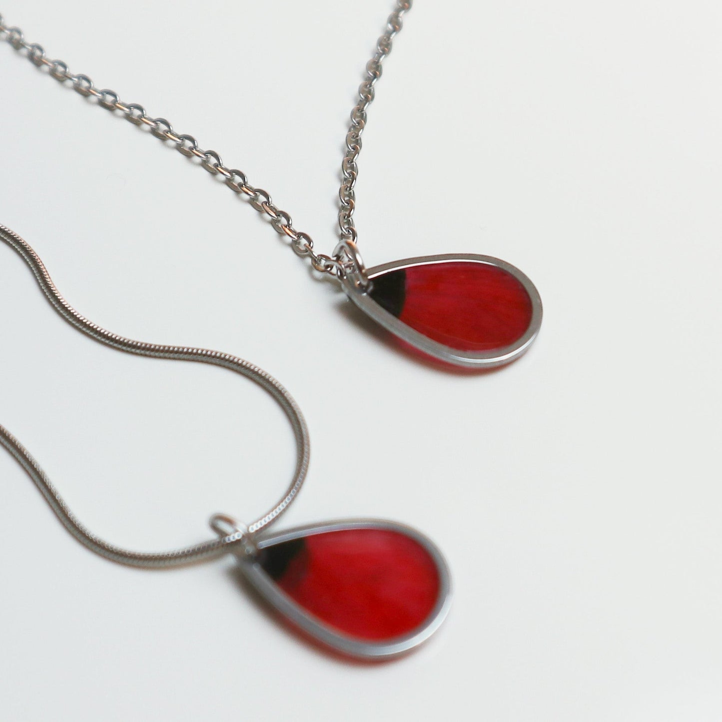 Drupt zilveren druppelvormige ketting met echte rode klaproos bloemblaadjes in een minimalistisch design.