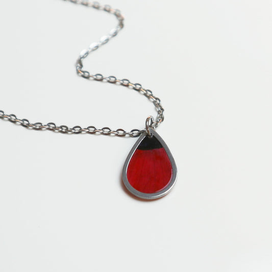Drupt zilveren ketting met druppelvormige hanger waarin een rode klaproos verwerkt is, minimalistisch design.