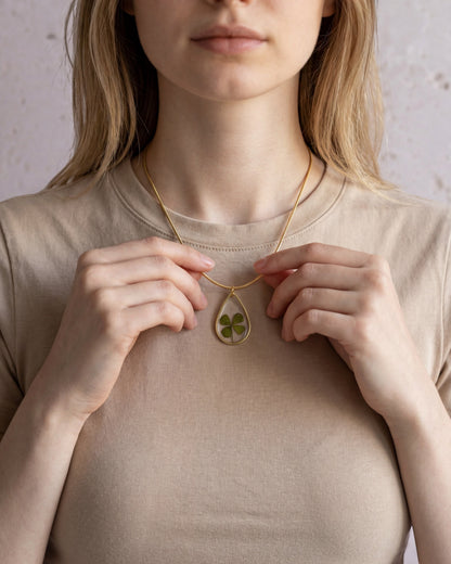 Drupt zilveren druppelvormige hanger met echt klavertjevier gedragen door een vrouw aan een subtiele ketting