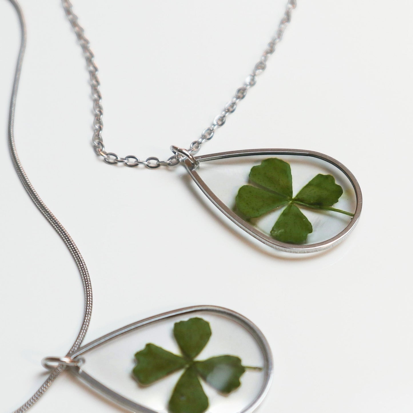 Drupt zilveren druppelvormige ketting met een echt klavertjevier in een minimalistisch handgemaakt sieraad