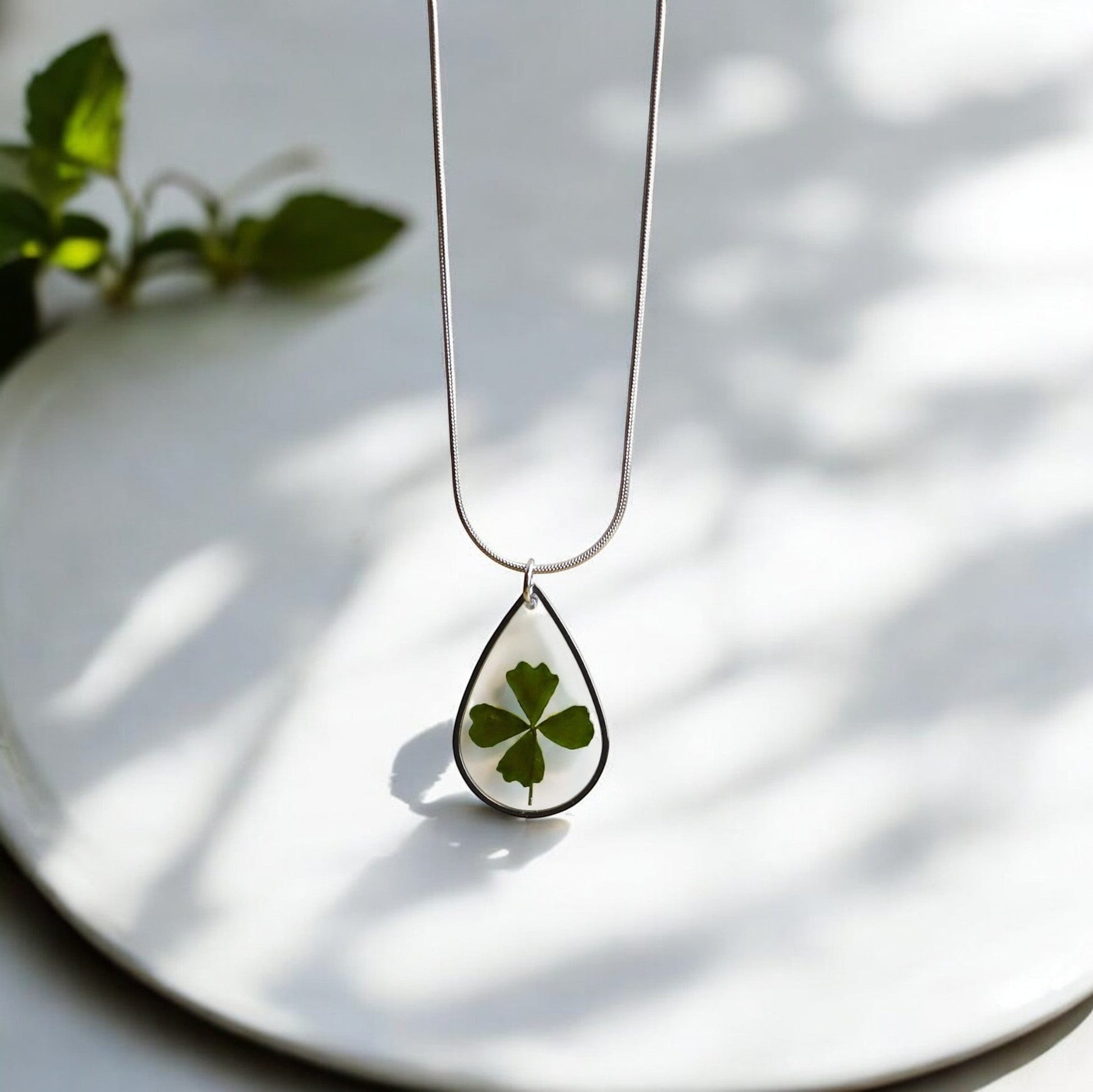Drupt zilveren druppelvormige ketting met een echt klavertjevier in hars, minimalistisch en handgemaakt sieraad.