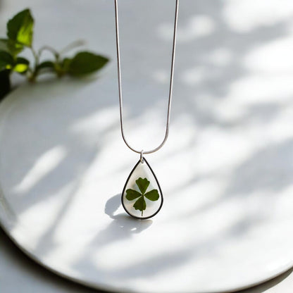 Drupt zilveren druppelvormige ketting met een echt klavertjevier in hars, minimalistisch en handgemaakt sieraad.