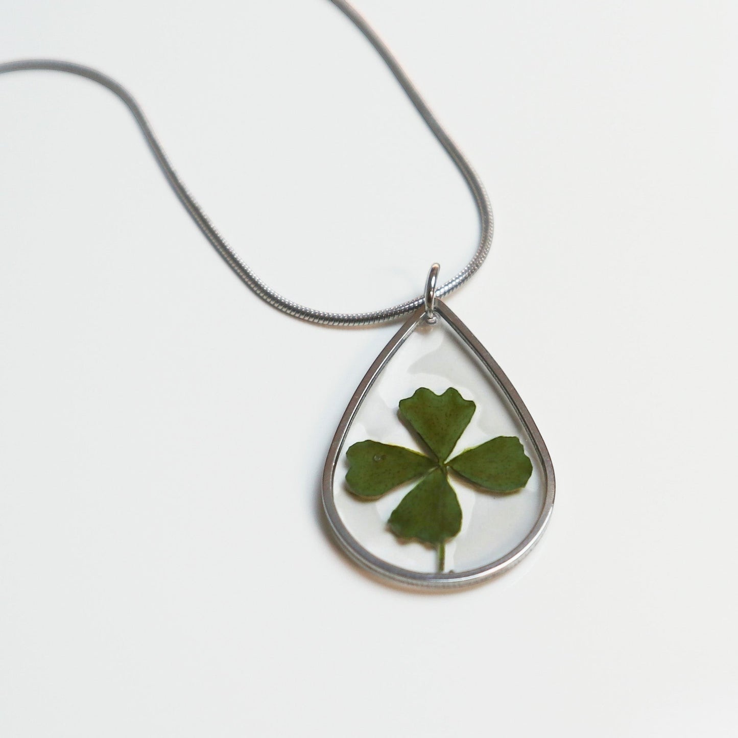 Drupt zilveren druppelvormige ketting met een echt klavertjevier in hars, minimalistisch handgemaakt sieraad.