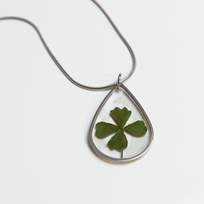 Drupt zilveren druppelvormige ketting met een echt klavertjevier in hars, minimalistisch handgemaakt sieraad.